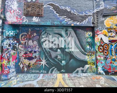 Ghent-East Flanders-Belgium-February 9, 2020,Complex layering of graffiti and street art on a distressed brick wall and metal security shutter in an u Stock Photo