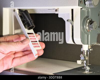 Adjusting a Vintage Sewing Machine Close-Up; Close-up shot of a person's hand setting up or repairing an older, classic sewing machine. Focus on the m Stock Photo