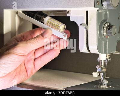Adjusting a Vintage Sewing Machine Close-Up; Close-up shot of a person's hand setting up or repairing an older, classic sewing machine. Focus on the m Stock Photo