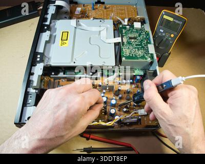 Hands Testing Electronic Circuit Board with Multimeter; Close-up of technician's hands using a multimeter to diagnose or repair complex electronic cir Stock Photo