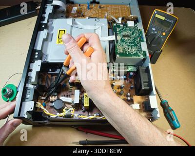 Hands Testing Electronic Circuit Board with Multimeter; Close-up of technician's hands using a multimeter to diagnose or repair complex electronic cir Stock Photo