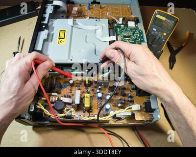 Hands Testing Electronic Circuit Board with Multimeter; Close-up of technician's hands using a multimeter to diagnose or repair complex electronic cir Stock Photo
