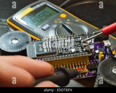Engineer testing microcontroller board.; Close-up of an engineer testing voltage on a modern microcontroller development board (PCB) using a digital m Stock Photo