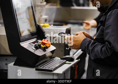 Factory technician using data collection device to log operations on CNC control console with digital display and manual controls Stock Photo