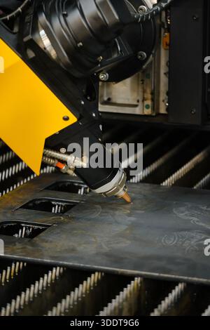 Close-up of fiber laser cutter nozzle and head assembly during high-speed sheet metal profile cutting on CNC flatbed table Stock Photo