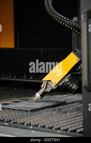 Close-up of fiber laser cutter nozzle and head assembly during high-speed sheet metal profile cutting on CNC flatbed table Stock Photo