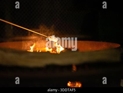 Marshmallow roasting over an open fire pit at night, capturing a cozy outdoor moment of relaxation and simple pleasure Stock Photo