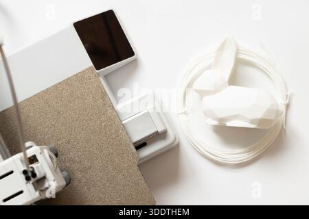 Desktop 3D printer and white low-poly rabbit and filament on white background, modern additive manufacturing technologies Stock Photo