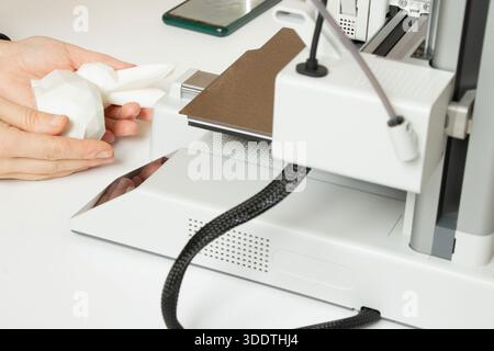 A desktop 3D printer and a white low-poly bunny on the printer, along with female hands, modern technologies for additive manufacturing Stock Photo