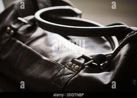 Close-up view of dark leather bag focusing on handle, strap attachment, and metal hardware. Natural leather texture, stitching, craftsmanship, premium Stock Photo