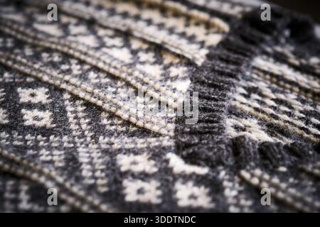 Macro close-up of knitted sweater showing detailed woven texture, ribbed collar, and geometric pattern. Textile structure, fabric depth, cozy material Stock Photo