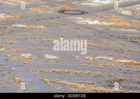 Dirty orange slush and tire tracks on a wet winter road. Stock Photo