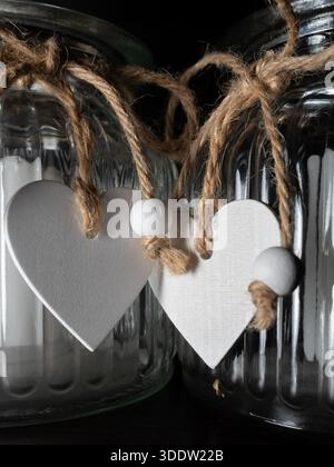 Close-up of clear glass jars tied with rough twine, featuring white heart shapes. Perfect for rustic home decor, craft projects, gift packaging, and s Stock Photo