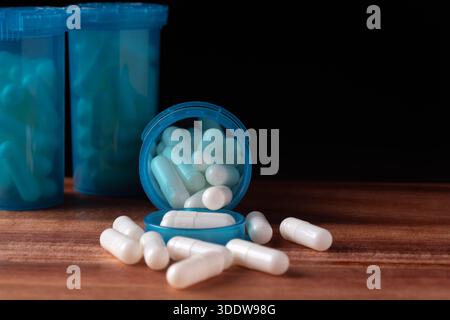 A blue container with white pills is placed on a wooden table. The pills are scattered around the container, creating a sense of disorder and disarray Stock Photo