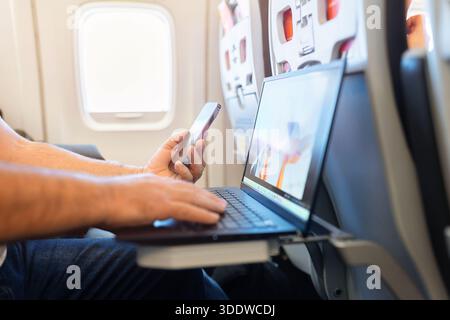 Passenger using smartphone and laptop simultaneously during airplane flight Stock Photo