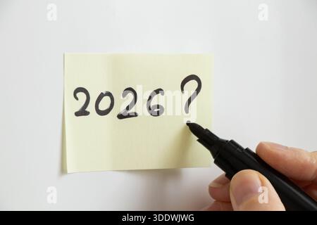 The year 2026 and a question mark written in black marker by a girl on a yellow sheet of paper taped to a white wall, a concept for the beginning of a Stock Photo