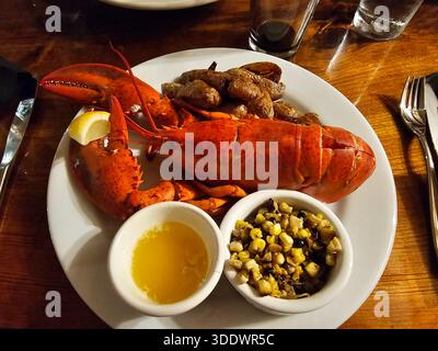 Whole cooked lobster seafood on dinner plate with side dishes at restaurant table Stock Photo