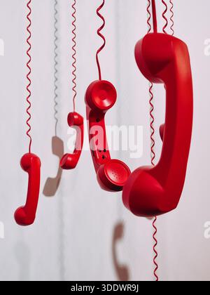 Close-up of red retro handsets on coiled cords. A vertical shot of several bright red vintage telephone receivers hanging by their spiral cords. Stock Photo