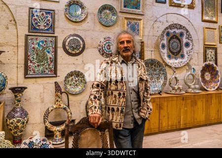 Master potter Galip stands in front of painted ceramic plates and vases at Çeç Pottery Chez Galip in Avanos İlçe Merkezi. Central Anatolia Region, Turkey Stock Photo