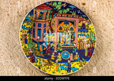 A colourful ceramic plate from Chez Galip Pottery (Çeç Pottery) in Avanos, Turkey, depicts an Ottoman court scene: an enthroned ruler surrounded by servants, musicians and animals, painted in bold blue, yellow and red. Since 1979, the workshop has also run the adjoining Hair Museum, where locks from more than 13,000 women hang. Stock Photo