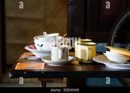 Kedah, Malaysia, December 5, 2025: Assorted vintage enamelware and ceramic dishes with food remnants on a rustic wooden cafe table after dining. Stock Photo