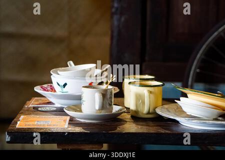 Assorted vintage enamelware and ceramic dishes with food remnants on a rustic wooden cafe table after dining. Stock Photo