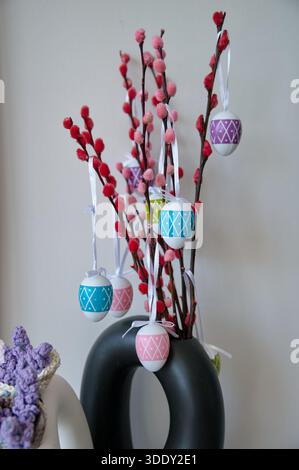 Vase with branch and Easter eggs against white wall Stock Photo