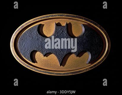 A detailed textured gold and black oval emblem representing a Batman emblem against a black background. Stock Photo