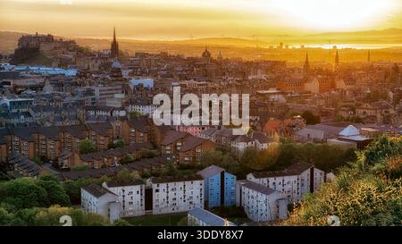 Panoramic sunset view over the city of Edinburgh from Arthurs Seat hill, with warm evening light, historic architecture and urban landscape blending w Stock Photo