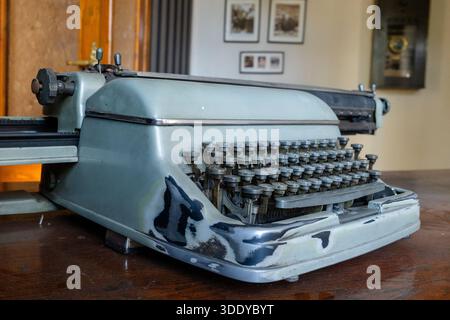 Old mechanical typewriter placed on a wooden desk in a historic office interior with classic furnishings. Stock Photo
