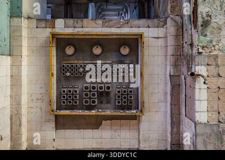Wide view of abandoned factory interior wall with old electrical switchboard and damaged tiled surfaces. Stock Photo