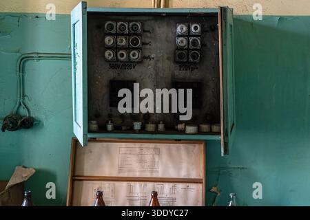 Old abandoned electrical control cabinet with ceramic fuses and wiring mounted on deteriorated interior wall. Stock Photo