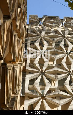 Layered facade featuring white concrete stars and warm wooden panels creating rhythmic shadows in daylight. Stock Photo