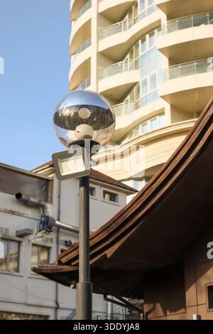 Sleek contemporary apartment tower with flowing curved facade, expansive glass balconies, and reflective surfaces capturing clear blue skies against a Stock Photo