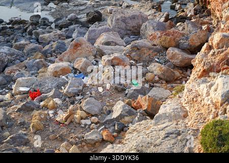 Environmental pollution concept showing plastic bottles, bags, and trash discarded among coastal rocks. Human impact on the ecosystem. Stock Photo