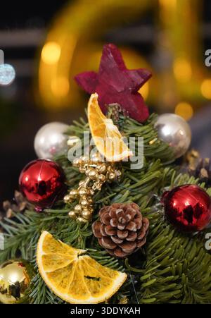 Vertical close-up of a miniature Christmas tree decorated with pine cones, red and gold baubles, and dried orange slices. Stock Photo