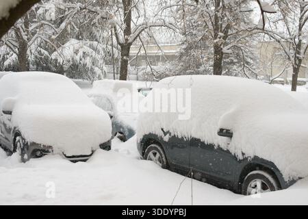 Snow covered parked cars are fully buried under thick snow after heavy winter snowfall in a residential area. Stock Photo
