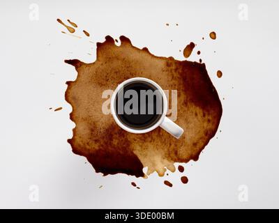 Coffee cup spilling dark beverage, forming a large brown stain and splatters on a clean white surface from above Stock Photo