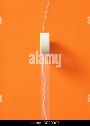 Clear adhesive tape unrolling, mending a white torn paper stripe on a vibrant orange surface, symbolizing repair, fixing and solutions Stock Photo