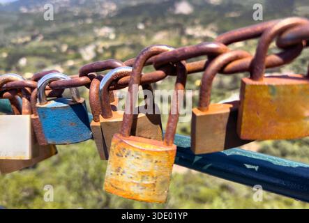 Love lock concept. Weathered padlocks hang on the rusty chain above a green valley in Corfu, Greece. Sunny summer day Stock Photo