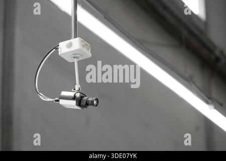 A ceiling-mounted surveillance camera installed on a metal conduit inside an industrial or commercial interior. Copy space Stock Photo