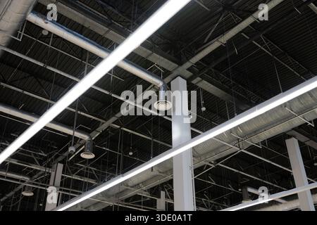 Industrial ceiling with exposed ventilation ducts, metal beams, and linear LED lighting inside a modern commercial or industrial building. Stock Photo