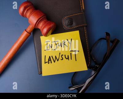The image displays a legal concept represented by a gavel, glasses, notebook, and a sticky note with the text INJURY LAWSUIT. Stock Photo