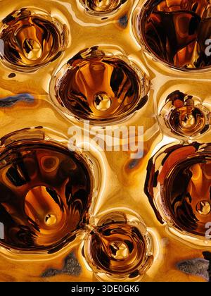 Molten gold texture with fluid reflective depressions. A high-gloss, macro view of a decorative gold-colored panel featuring large circular dimples. Stock Photo
