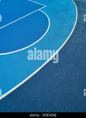 Blue basketball court: high-angle abstract view of markings and texture. Layered blue tones on textured athletic surface with white curves. Stock Photo