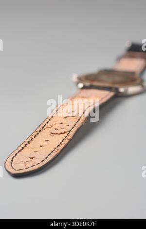 used brown leather wristwatch strap isolated neutral gray background, cracked and peeling inner surface damaged leather material, close-up Stock Photo
