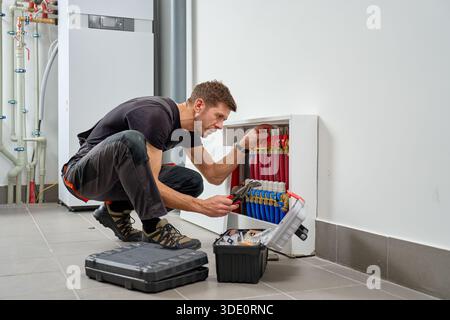 Technician inspecting underfloor heating manifold with pipes and valves in utility room. Concept of heating installation, plumbing maintenance, HVAC service and residential energy system Stock Photo