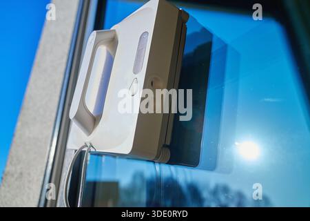 Square window cleaning robot washing glass. Robotic window cleaner working on window surface against blue sky. Smart home appliance concept Stock Photo