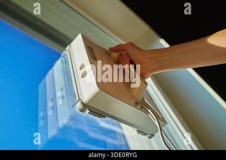 Woman starting robotic window cleaner on glass surface of window. Using automatic device for window cleaning at home. Smart home appliance concept Stock Photo