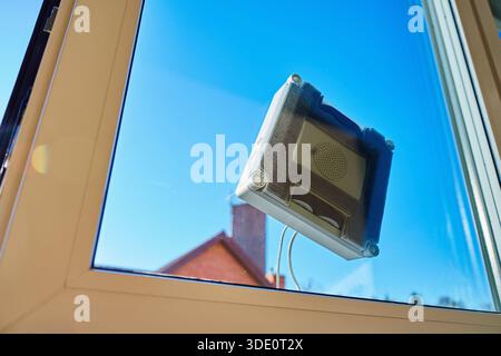 Square window cleaning robot washing glass. Robotic window cleaner working on window surface against blue sky. Smart home appliance concept Stock Photo